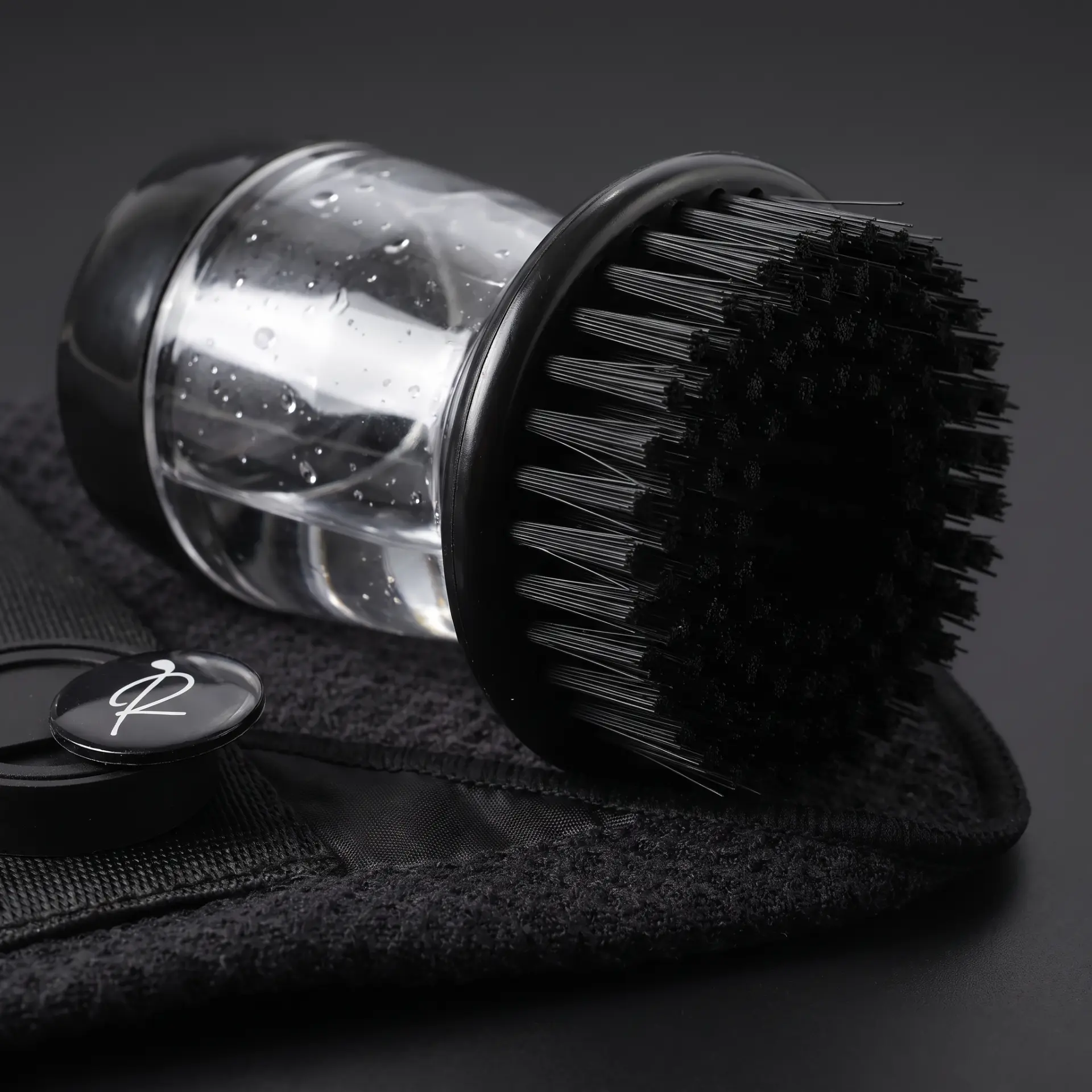 Close-up of the Ryft brush tool with its clear refillable water reservoir sitting on a black waffle-weave golf towel