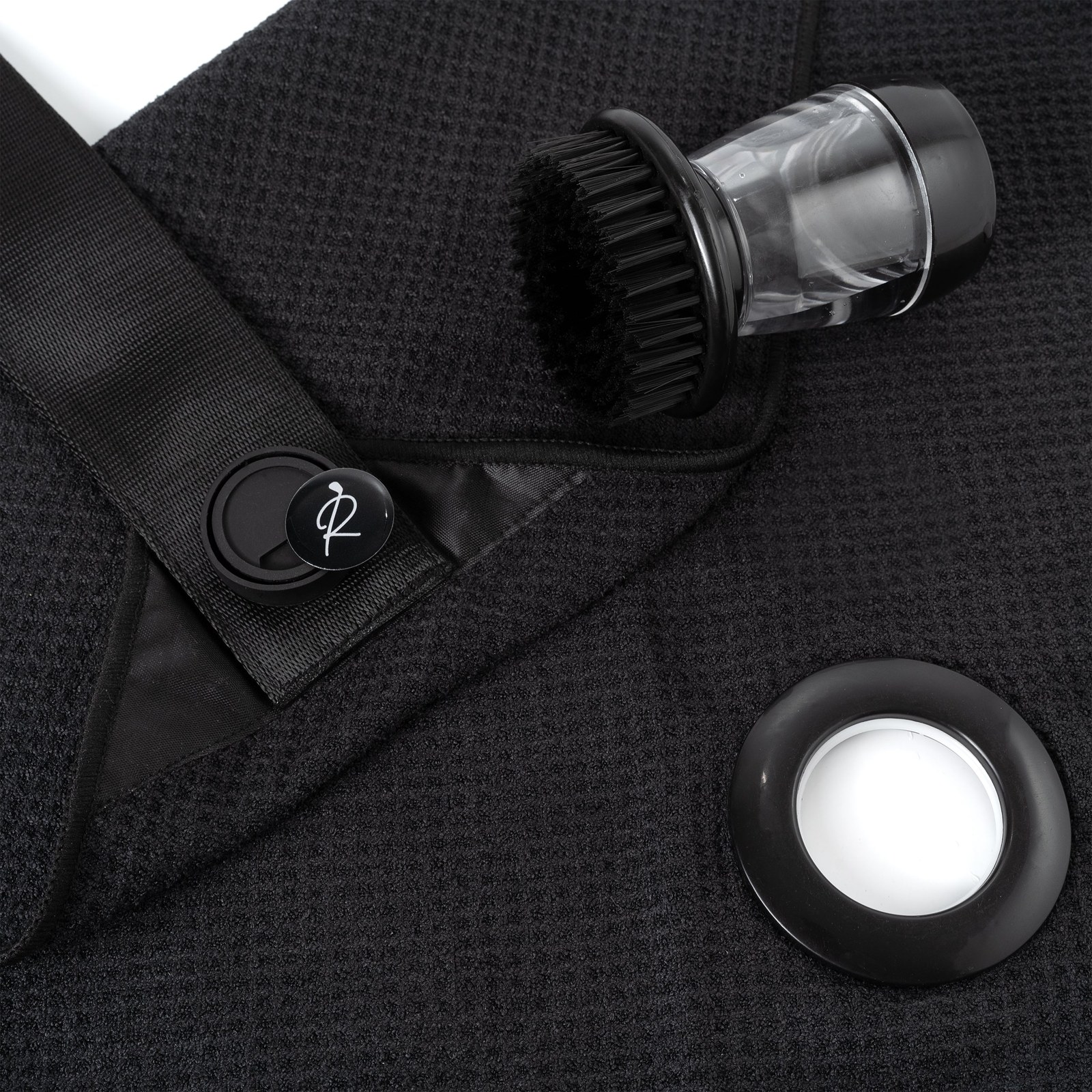 Macro photograph of black waffle-weave microfiber, showing the raised grid of pockets next to the flat satin corner panel and webbing strap
