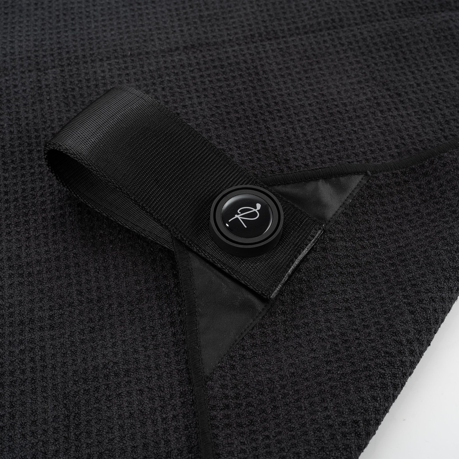 Macro shot of black waffle-weave microfiber fabric, showing the raised grid of absorbent pockets beside a flat woven strap